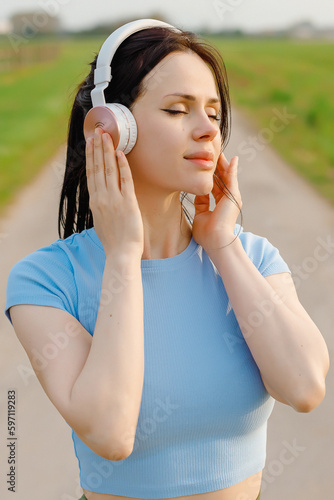 Portrait of smiling young  woman listening to music on headphones outdoors on city street.