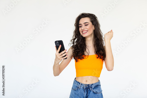 Portrait of a happy woman holding mobile phone and celebrating a win isolated over white background