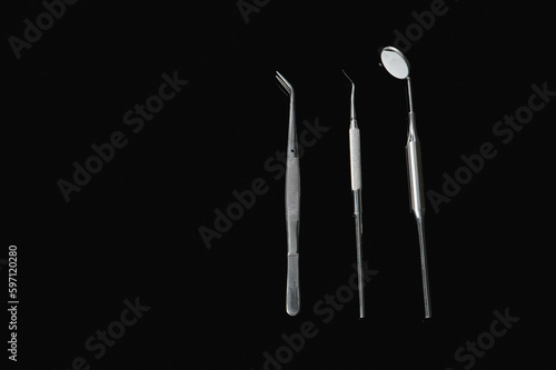 Dental mirror, dental probe, dental tweezers on black background. Professional dental tools for primary examination. Luxurious looking. Caries prevention and endo treatment