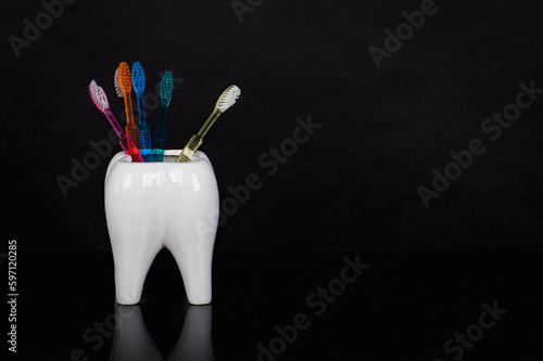 Disposable plastic toothbrushes in a ceramic tooth against a black background. Dental supplies for oral care