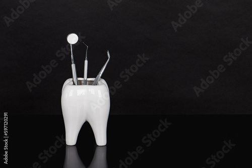 Dental mirror, dental probe, dental tweezers and ceramic tooth on black background. Professional dental tools for primary examination. Luxurious looking. Caries prevention and endo treatment