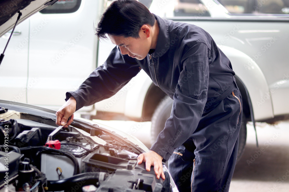 Asian handsome mechanic man in uniform working with engine vehicle, auto mechanic technician inspecting maintenance engine system of customer car automobile at garage car repair service workshop. Asian handsome mechanic man in uniform working with engine vehicle, auto mechanic technician inspecting maintenance engine system of customer car automobile at garage car repair service workshop.