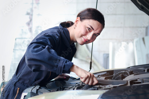 Beautiful female auto mechanic in uniform working with engine vehicle at garage, car service technician woman checking and repairing customer car at automobile service center, vehicle repair service.