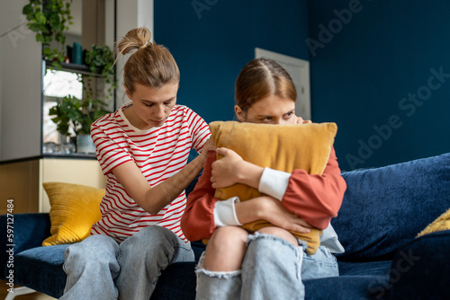 Loving supportive mother sitting on sofa with upset teenage girl, helping child through adolescence, talking with depressed anxious teen about bullying. Love and support in parent-child relationships