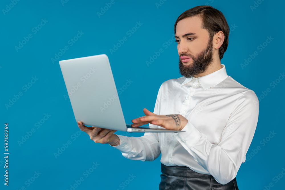 Brunette graceful transgender man wears white shirt working on portable computer typing on keyboard