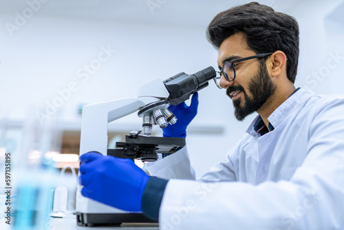 Smiling doctor working in modern laboratory research scientist examines substance under microscope.