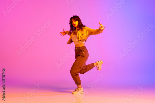 Dynamic image of young female dancer in sport style clothes dancing against gradient pink purple background in neon light. Concept of contemporary dance, youth, hobby, action and motion © master1305