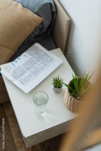 High angle view of glass of water and newspaper on bedside table in bedroom.