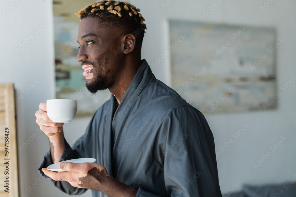 Smiling african american man with vitiligo holding cup of coffee at home. Smiling african american man with vitiligo holding cup of coffee at home.