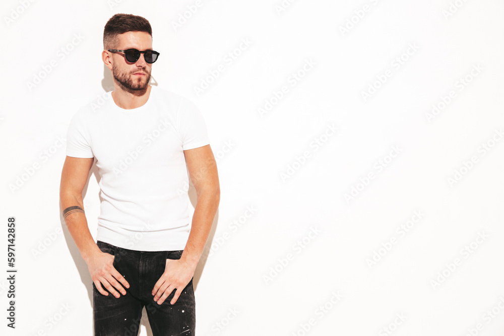Portrait of handsome smiling stylish hipster lambersexual model. Man dressed in white T-shirt and jeans. Fashion male posing in studio Portrait of handsome smiling stylish hipster lambersexual model. Man dressed in white T-shirt and jeans. Fashion male posing in studio