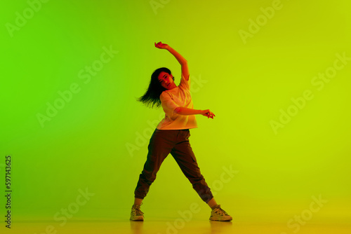 Dynamic image of young girl, female hip-hop dancer in motion against gradient green yellow background in neon light. Concept of contemporary dance, youth, hobby, action and motion © master1305