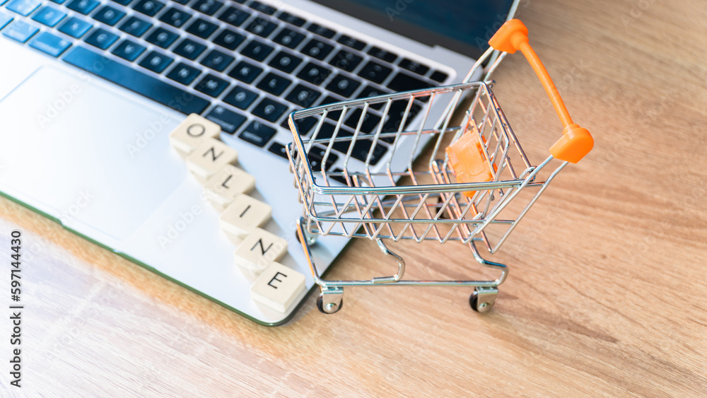 Online shopping concept. Shopping cart or trolley and laptop on wooden table.