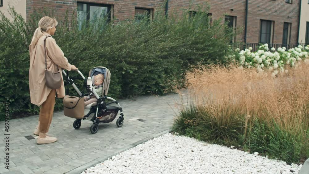 Tracking shot of young woman wearing comfortable casual outfit walking with her baby in stroller Tracking shot of young woman wearing comfortable casual outfit walking with her baby in stroller