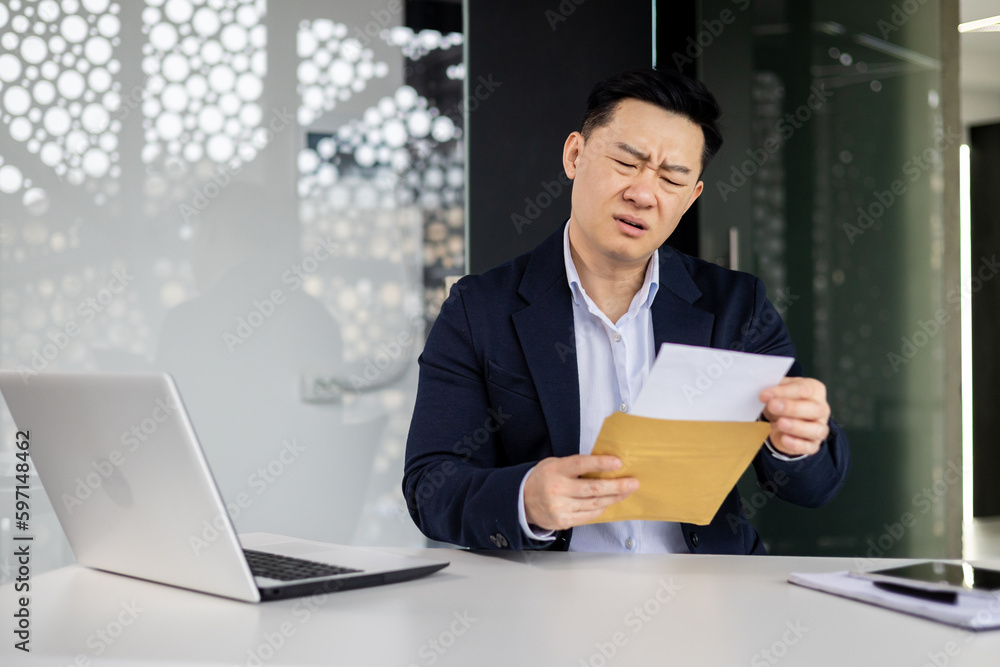 Frustrated and sad depressed businessman received mail envelope notification bad news, asian man at workplace inside office working with laptop, unhappy with achievement results. Frustrated and sad depressed businessman received mail envelope notification bad news, asian man at workplace inside office working with laptop, unhappy with achievement results.