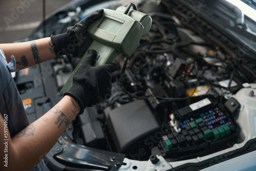 Car mechanic with a tattoo works under the hood