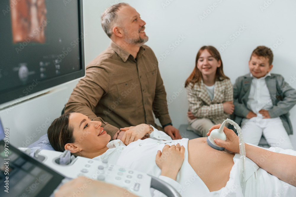Obraz premium Husband and kids are sitting together. Pregnant woman is lying down in the hospital, doctor does ultrasound