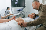 Happy husband is sitting and supporting his wife. Pregnant woman is lying down in the hospital, doctor does ultrasound