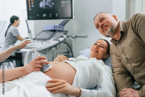 Husband is supporting his wife. Pregnant woman is lying down in the hospital, doctor does ultrasound