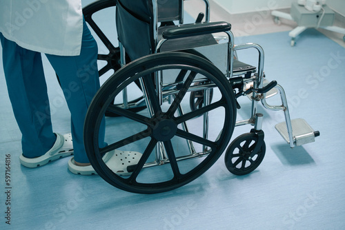 Uniformed nurse stands in a hospital corridor with a wheelchair