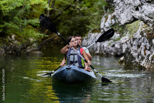 A young couple enjoying an idyllic kayak ride in the middle of a beautiful river surrounded by forest greenery