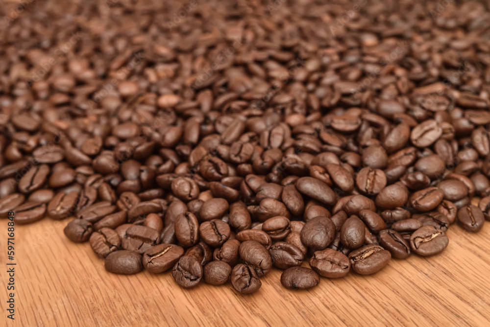 Heap of fresh roasted coffee beans on the brown wooden table. Close-up. Selective focus. 