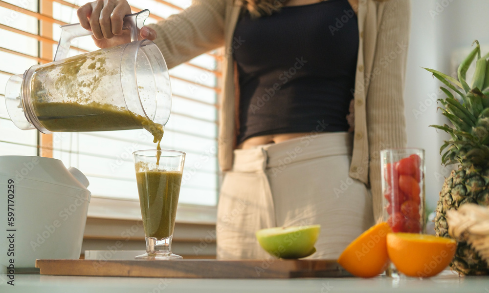 Healthy young woman pouring reen vegetable smoothie into a glass. Healthy eating, health, nutrition and vegetarian.