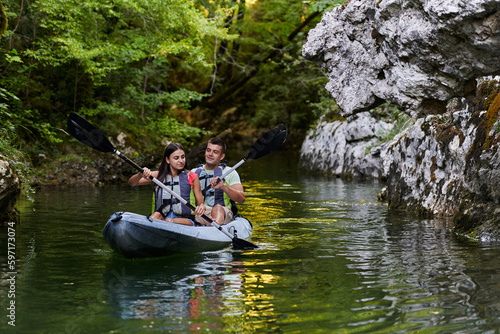 A young couple enjoying an idyllic kayak ride in the middle of a beautiful river surrounded by forest greenery © .shock