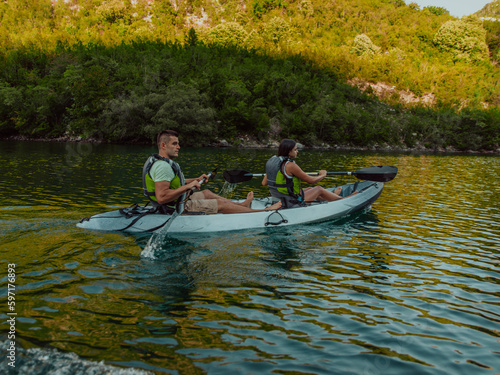 A young couple enjoying an idyllic kayak ride in the middle of a beautiful river surrounded by forest greenery