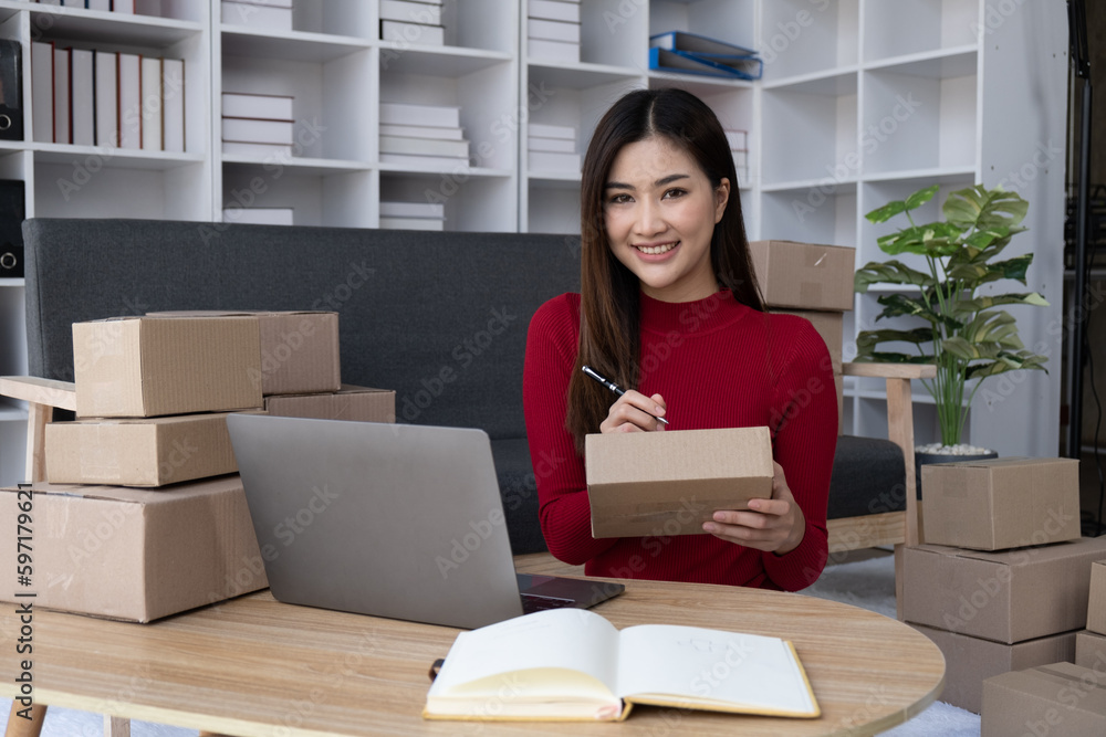 SME online business concept. Young online shop owner working in her roo, writing the customer address down on the boxes before distribute to the mail. SME online business concept. Young online shop owner working in her roo, writing the customer address down on the boxes before distribute to the mail.