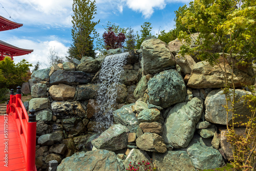 Vászonkép A lush green garden with a waterfall descending from rocky rocks.