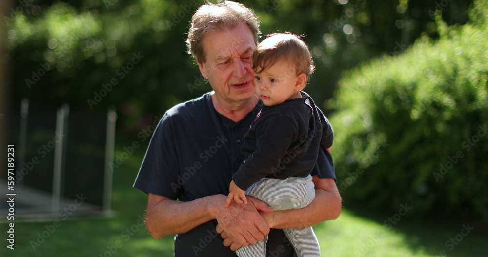 Fototapeta premium Senior man holding infant baby outside. Grand father bonding with toddler outdoors