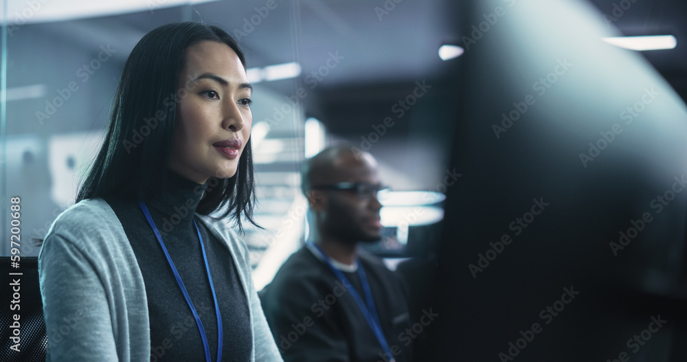 Beautiful Asian Female Working on a Desktop Computer in a Cyber Security Software Development Department. Positive Brunette Female Lightly Smiling While Working on a Project Beautiful Asian Female Working on a Desktop Computer in a Cyber Security Software Development Department. Positive Brunette Female Lightly Smiling While Working on a Project