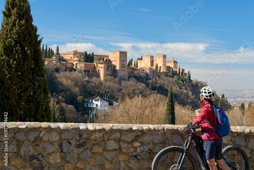 nice active senior woman cycling with her electric mountain bike in Granada below the world heritage site of Alhambra, Granada, Andalusia,  Spain