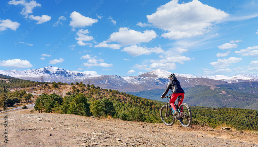 Fototapeta premium nice, active senior woman cycling with her electric mountain bike below the snow covered mountains of the Spanish Sierra Nevada, near Granada, Andalusia, Spain