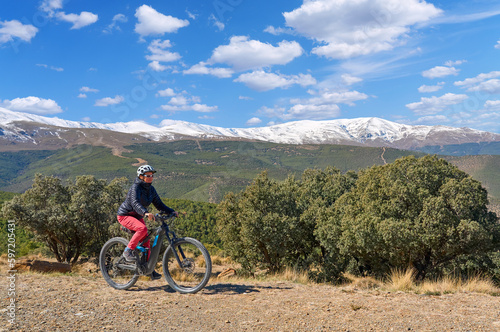 nice, active senior woman cycling with her electric mountain bike below the snow covered mountains of the Spanish Sierra Nevada, near Granada, Andalusia, Spain