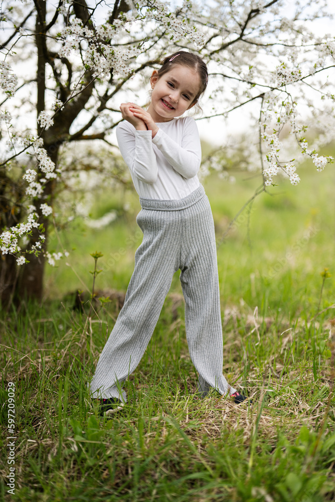 Portrait of preschool girl against white blloming tree in spring.
