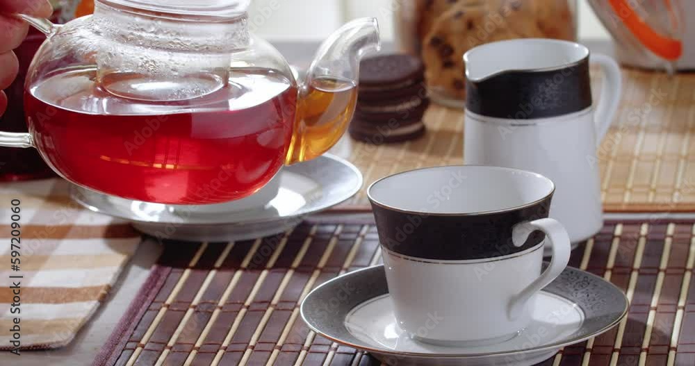Pouring Hot Black Tea Into a Cup Close-up. Fresh Hot Tea With Sweets on the Table, Healthy Morning. Black Hot Tea is Poured From a Glass Teapot Into a Cup, Slow Motion. 