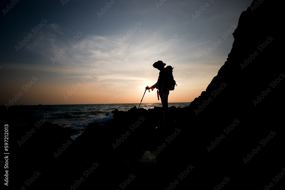 Hiker woman stands on the rock cliff against sunset at seaview ,hiking success silhouette in mountains,