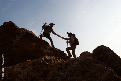 Hiking team hand to hand helping each other while climbing up on the mountain rock adventure travel concept