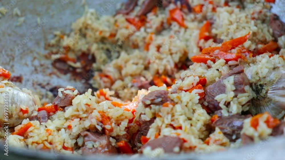The close -up of rice with lamb is interfered with a spoon. The cauldron of pilaf is prepared on fire. The male hand in the glove closes the hot cover. Hot dish in nature, lunch is ready. High quality The close -up of rice with lamb is interfered with a spoon. The cauldron of pilaf is prepared on fire. The male hand in the glove closes the hot cover. Hot dish in nature, lunch is ready. High quality