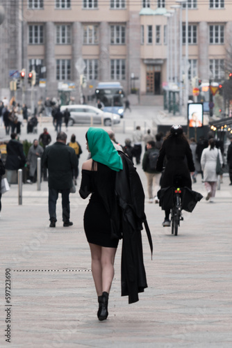 A woman with a perfect figure and red lips in a short black dress, a bright scarf on her head. Posing in the city