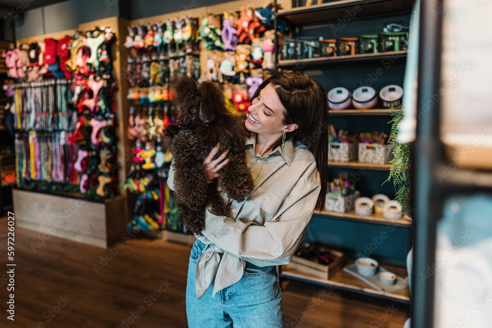 Beautiful young woman enjoying in modern pet shop together with her adorable brown toy poodle.