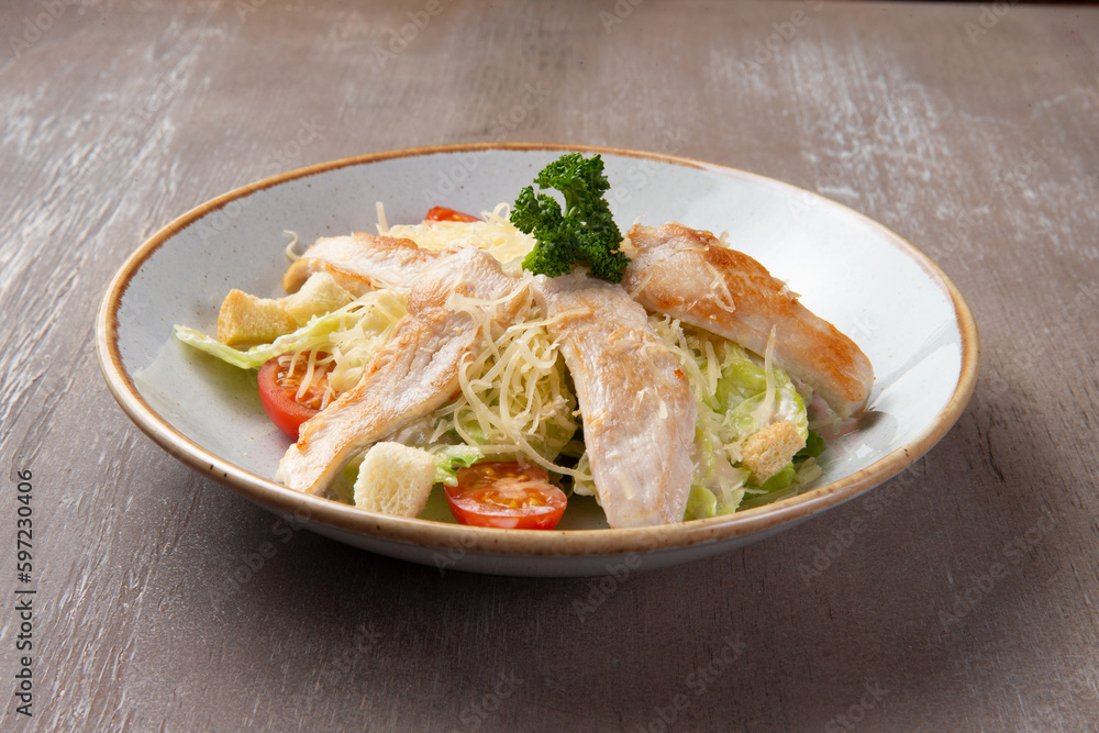 Salad with chicken fillet in a plate on a brown background.