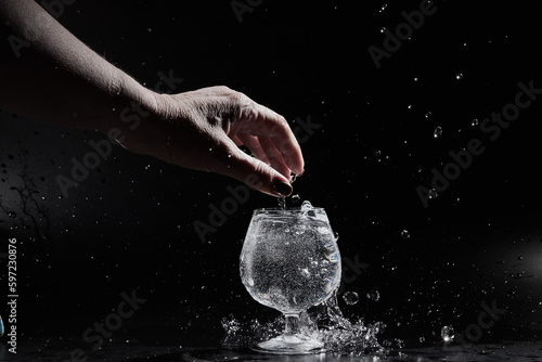 Fingers of hand of a woman touching water or mineral water in a wine glass on a black background