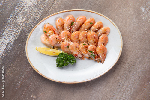 Cooked shrimp and lemon in a plate on a brown background.