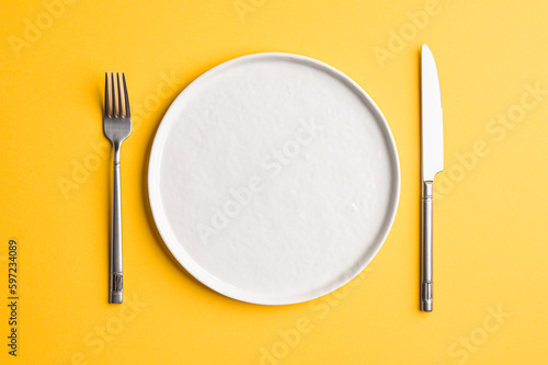 White flat empty plate with cutlery on a colored background. Top view.