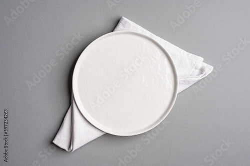 White flat empty plate and napkin on a light gray background.