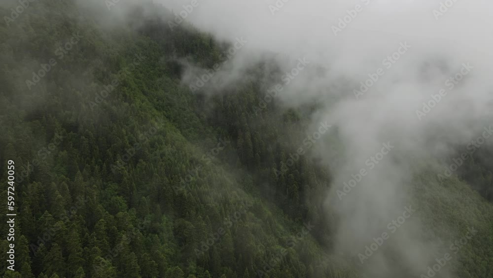Fog moving over mountain peaks, dramatic of weather conditions in the mountains, drone shot of cloud formations Fog moving over mountain peaks, dramatic of weather conditions in the mountains, drone shot of cloud formations