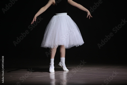 A ballet dancer in a position dancing in a white tutu and skirt on a black stage