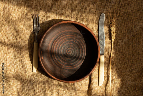 Clay plate and a knife with a fork on burlap, dishes and decor on the table, serving photo